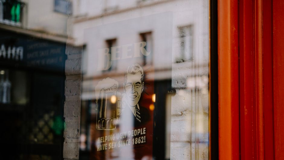 The image depicts an interior scene of a retail shopfront with exposed brick walls illuminated by warm lighting from a black, lantern-style ceiling fixture. A vertically oriented sale sign with red le